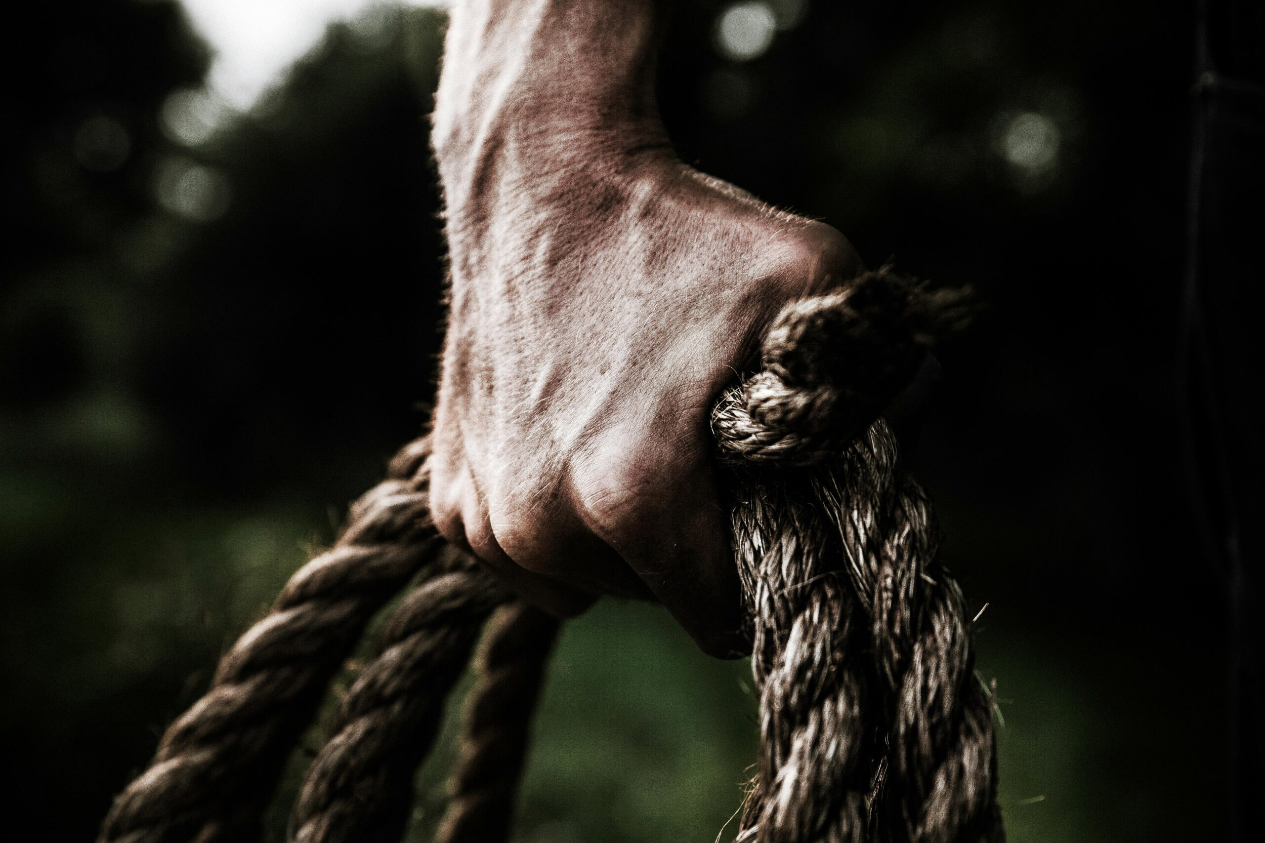 A close-up image shows a strong, firm hand gripping a thick, rough rope, showcasing strength and determination in an outdoor setting.