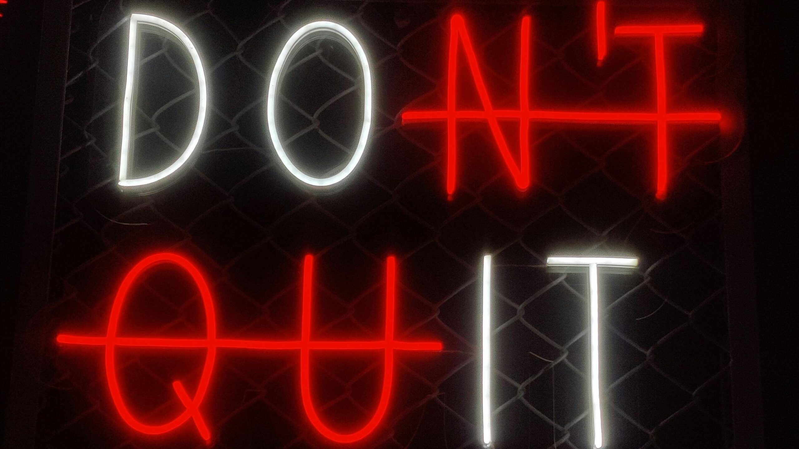 Illuminated 'Don't Quit' neon sign with motivational message in a dark background.