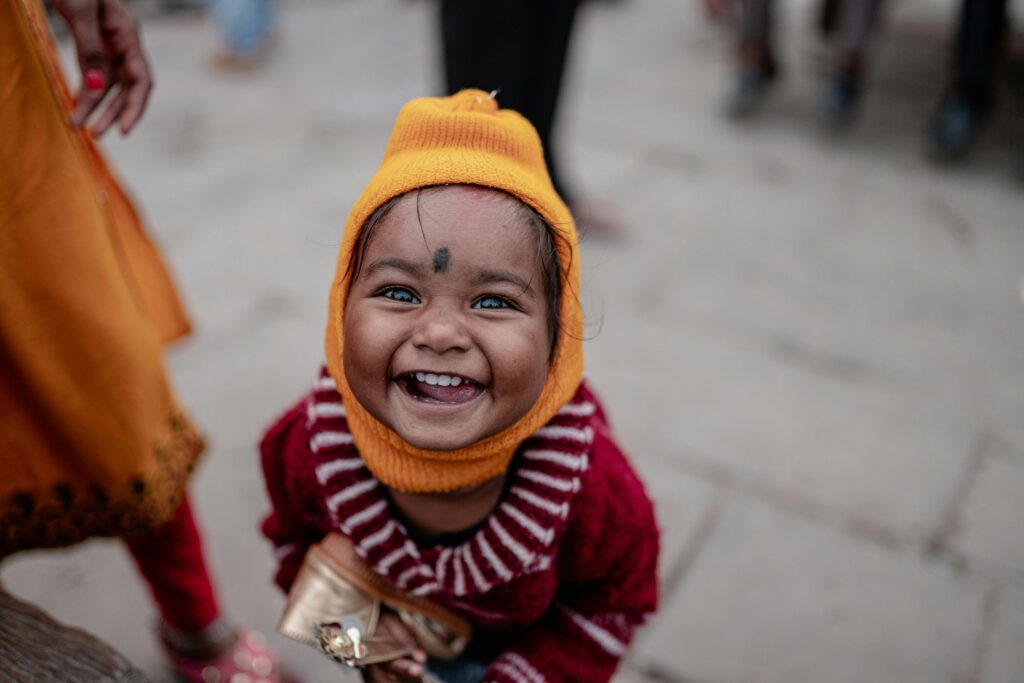 Adorable child beaming with joy in colorful winter clothing in Varanasi, capturing a moment of pure happiness.